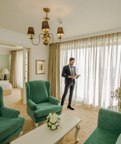 A gentleman holding a tablet in the living area at a Kingsbury Hotel room