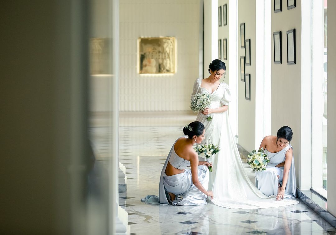 Two bridesmaids adjust the bride's saree in a bright hallway