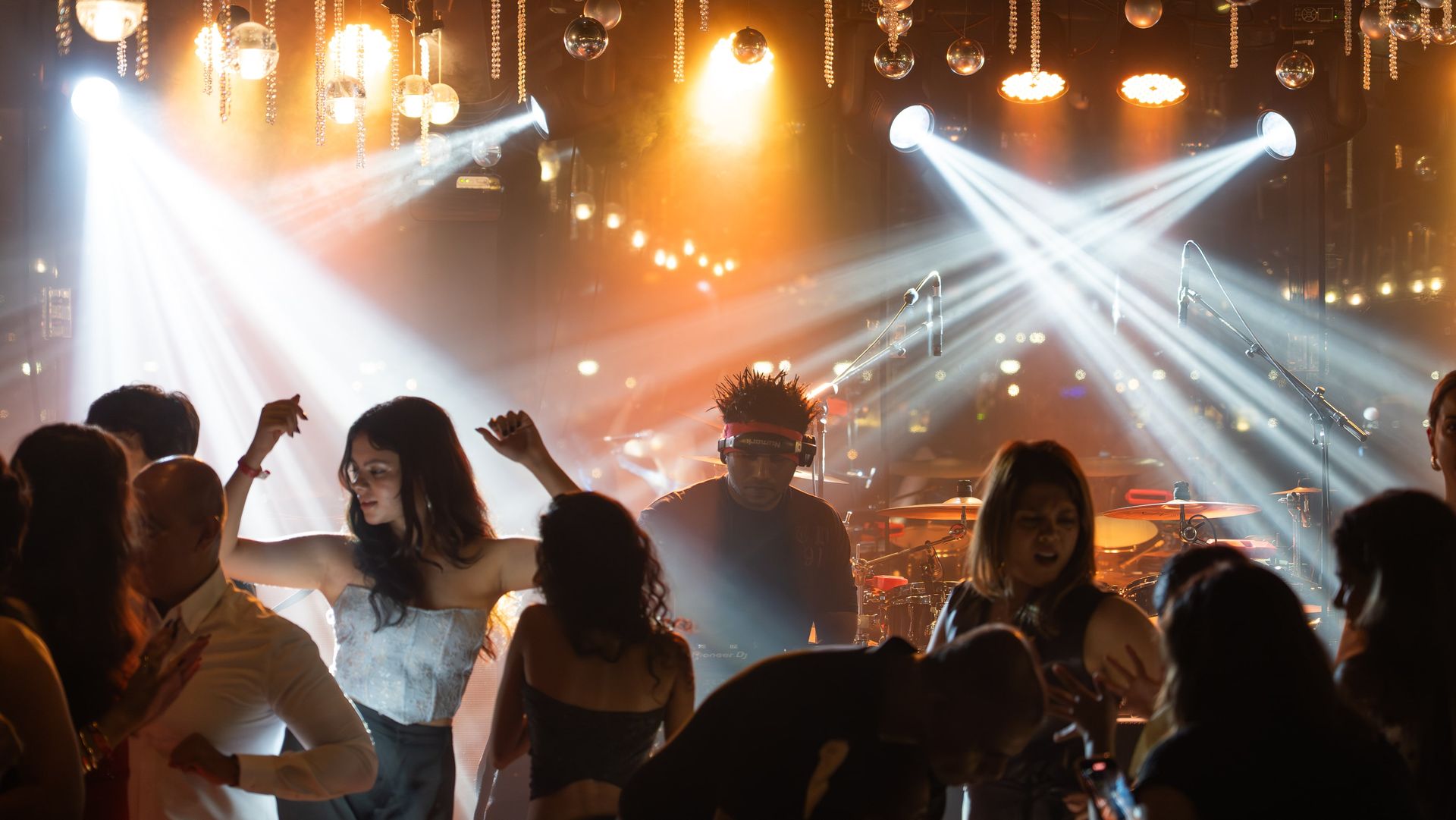 A DJ wearing headphones is performing for a crowd while people dance