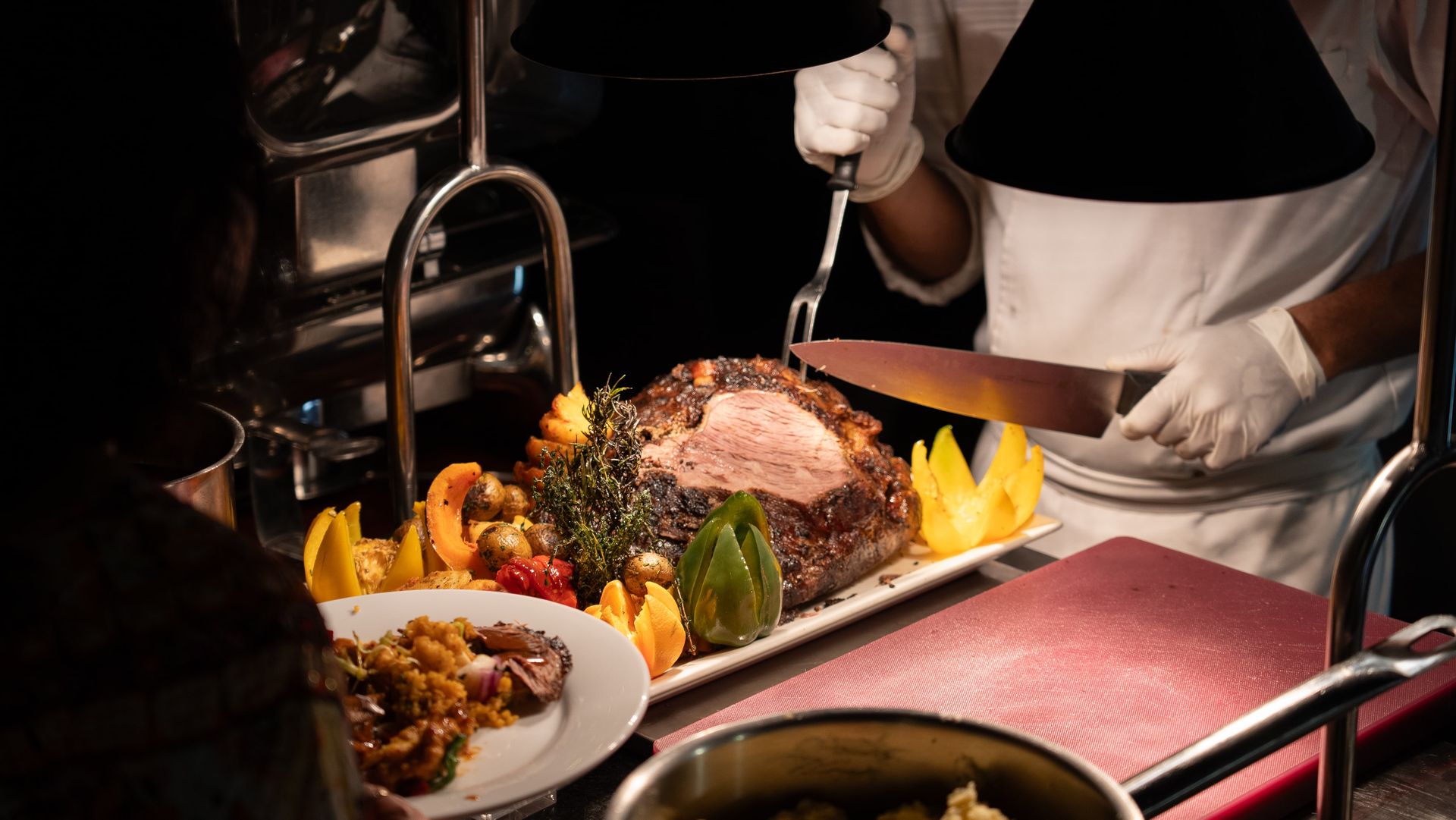 A chef carving a roasted cut of meat on a platter garnished with vegetables